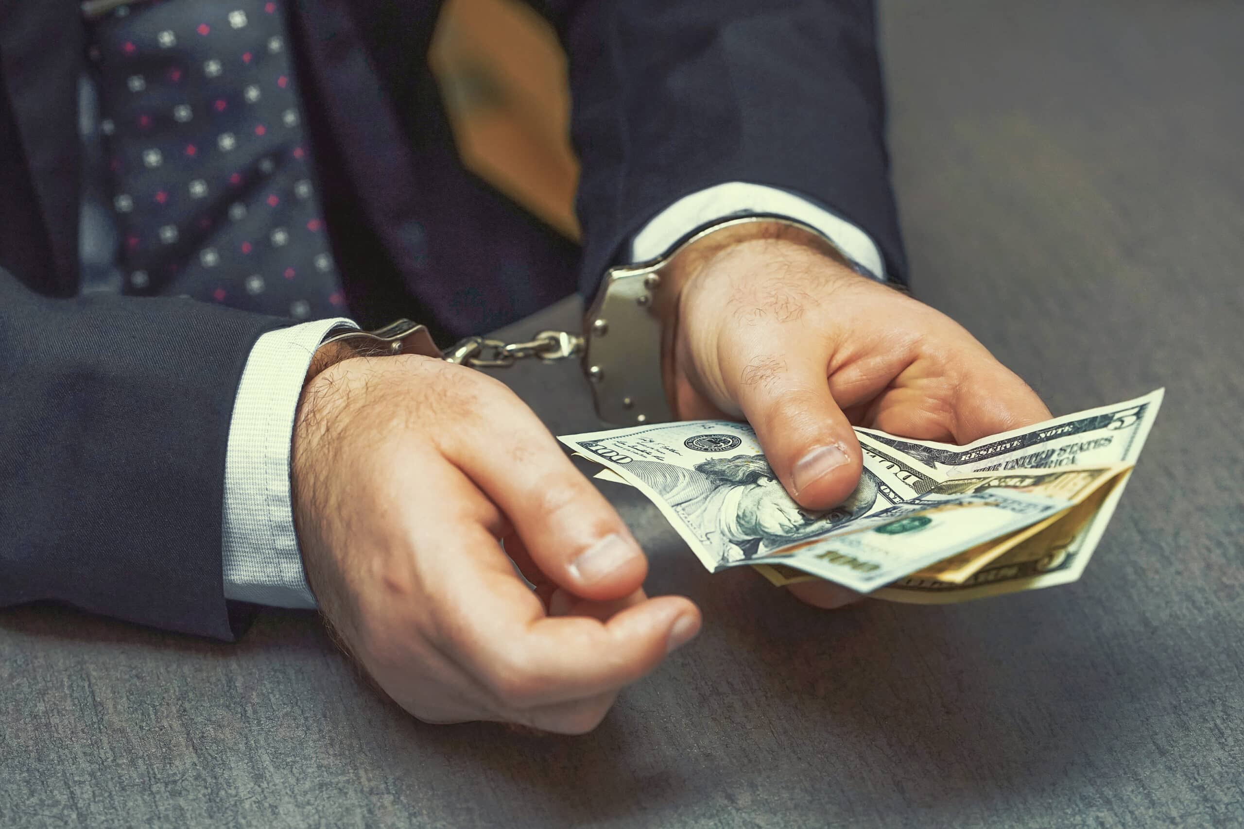 Photo of businessman in handcuffs holding bribe at desk, closeup. He should have called a wage and hour attorney in san diego.